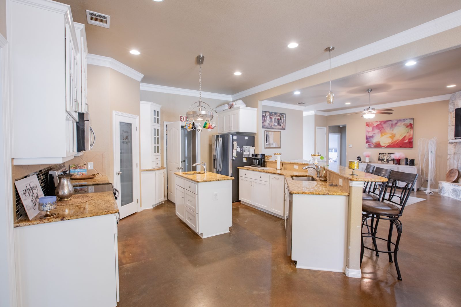 White kitchen with granite counters, a center island, breakfast bar with stools and a pantry, open to the living room