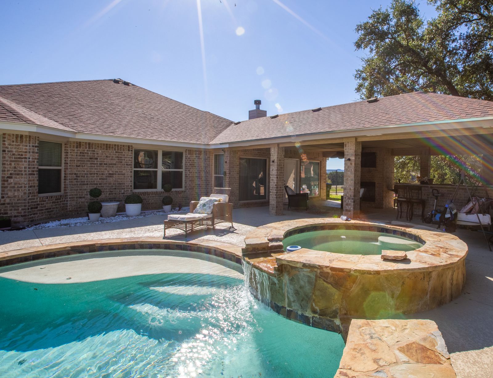 Stone jacuzzi with a waterfall spilling into the pool, lounge chair and covered patio behind